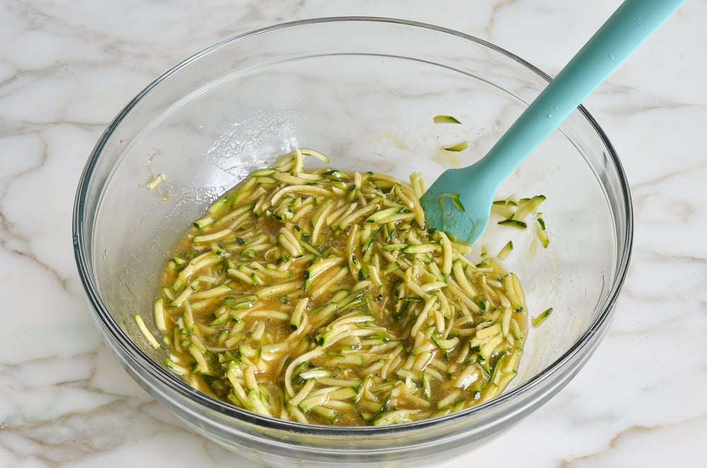 Shredded zucchini and liquid ingredients in a mixing bowl.