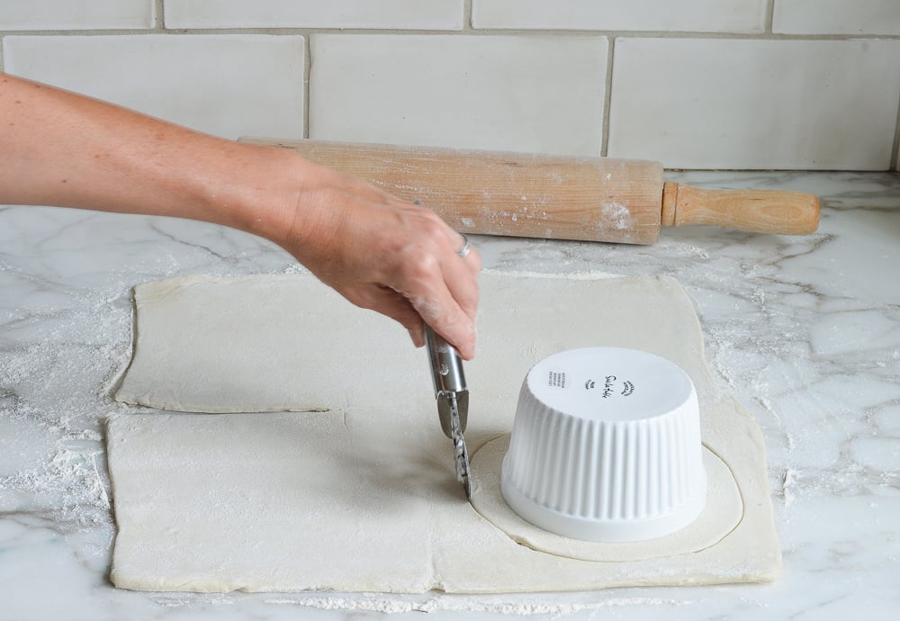 Person cutting out a circle of puff pastry dough.