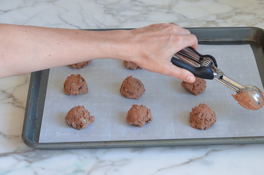 Person dropping balls of cookie dough onto a lined baking sheet.