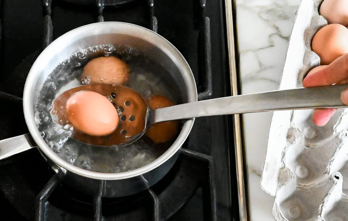 Lowering eggs into boiling water.