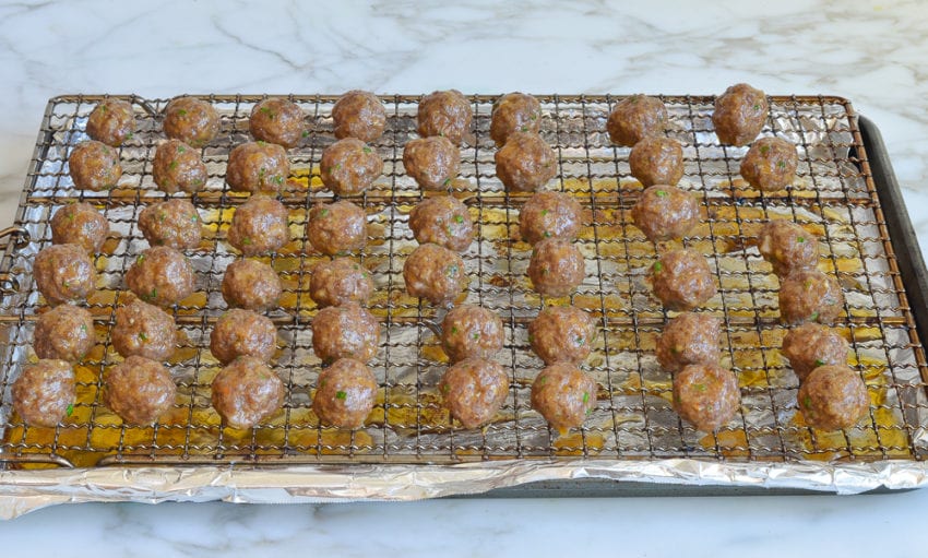 Cooked meatballs on a wire rack over a lined baking sheet.