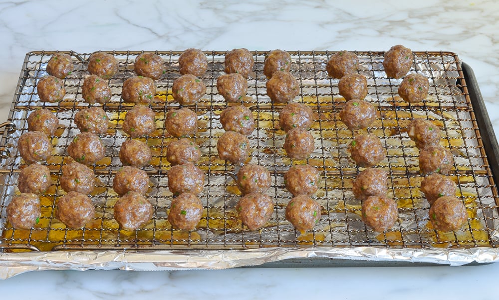 Cooked meatballs on a wire rack over a lined baking sheet.