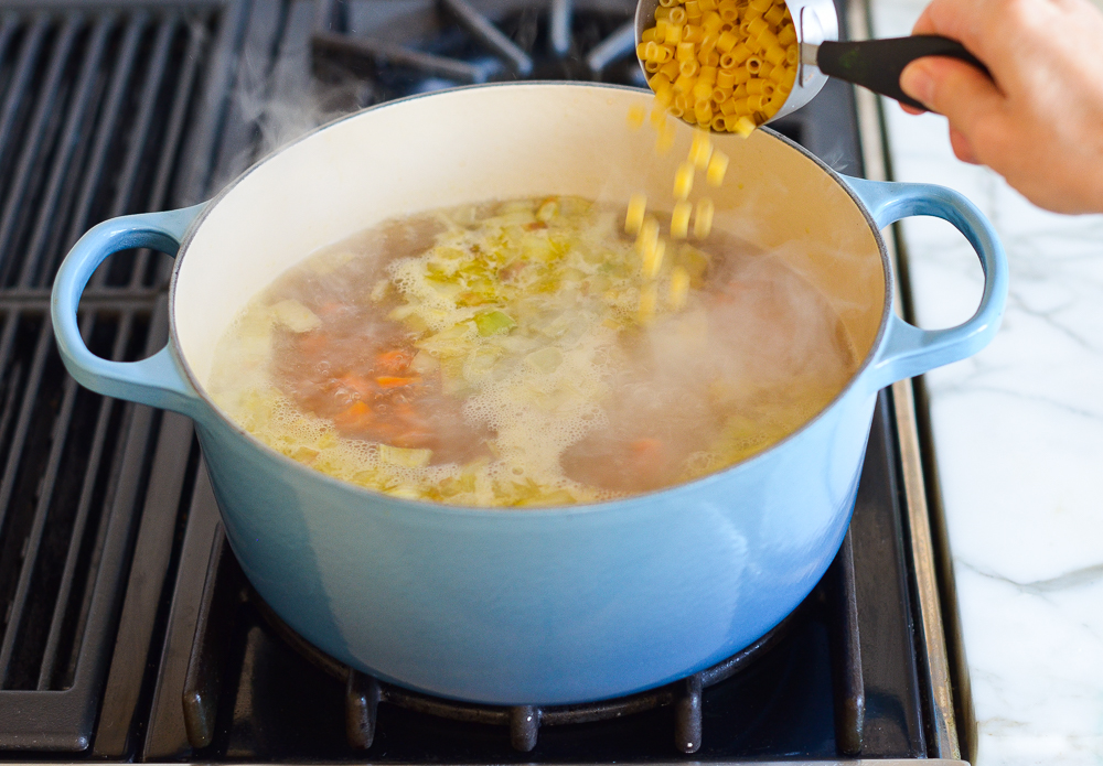 Boodles pouring into a Dutch oven of broth.