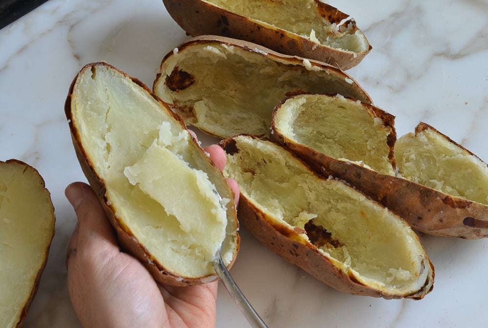 Person scooping the flesh from halved potatoes.
