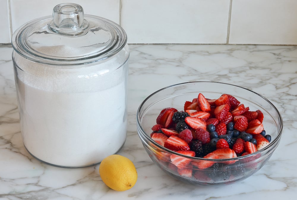 Sugar, lemon, and bowl of berries on a counter.