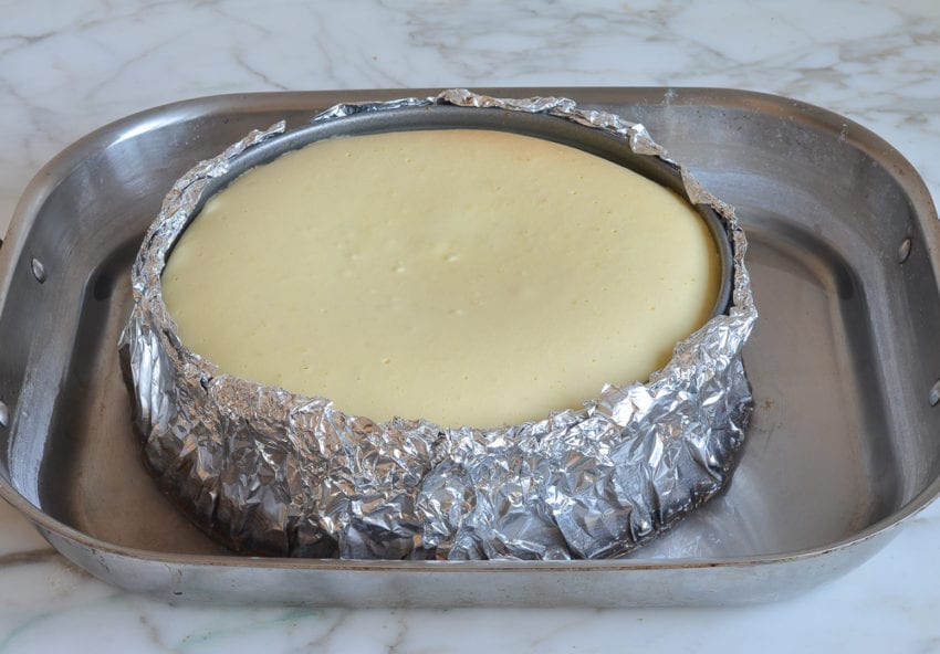 Cooked cheesecake in a springform pan wrapped in aluminum foil.