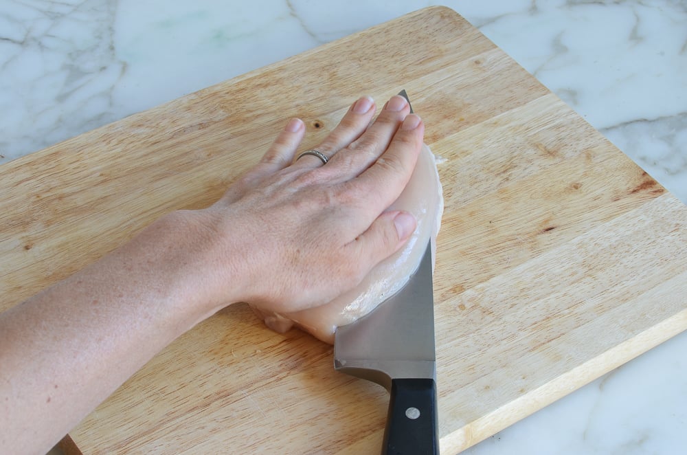 Person slicing a chicken breast with a large knife.