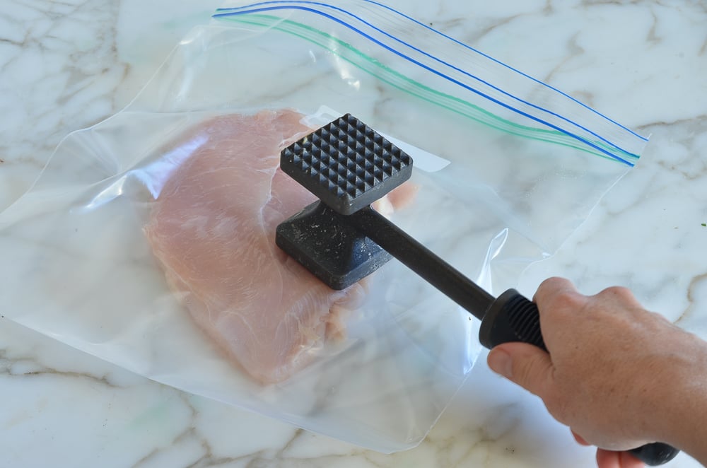 Person pounding a chicken breast with a meat mallet.