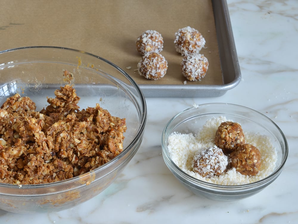 Balls of energy bite dough being rolled in coconut.