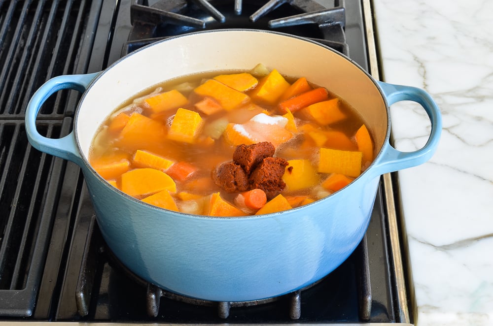Butternut squash and other ingredients in a Dutch oven of broth.