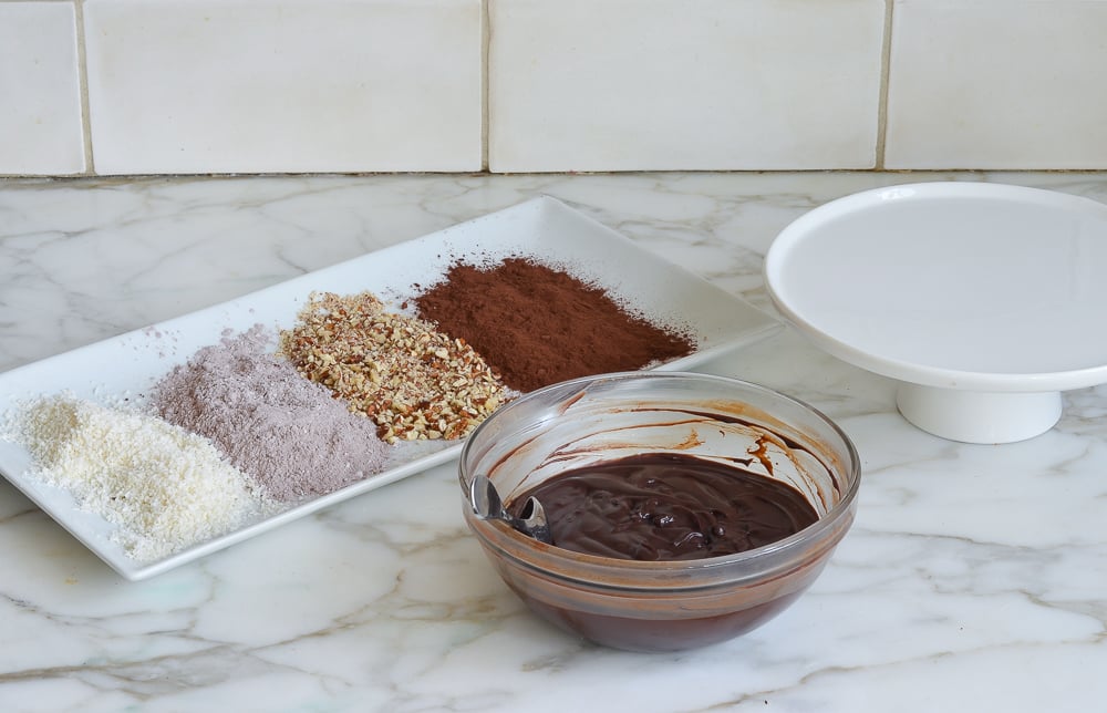 Bowl of chocolate next to a plate of truffle coatings.