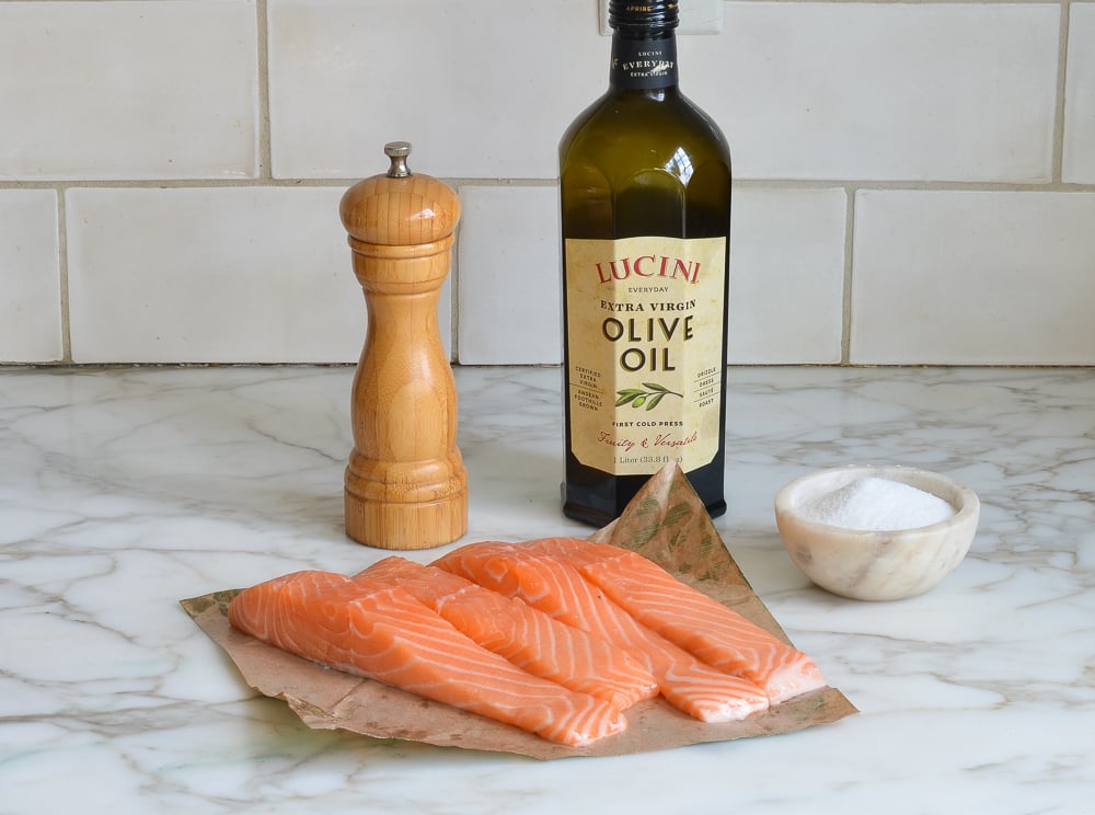 Salmon, olive oil, salt, and pepper on a counter.
