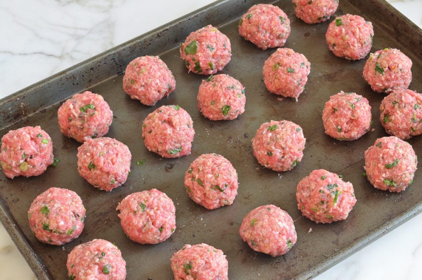 Baking tray of uncooked meatballs.