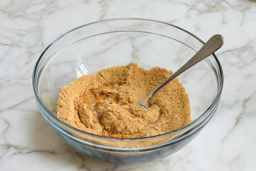 Melted butter in a bowl with graham cracker crumbs and sugar.