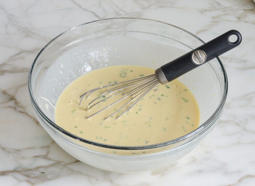Whisk in a bowl with a cheese and egg mixture.
