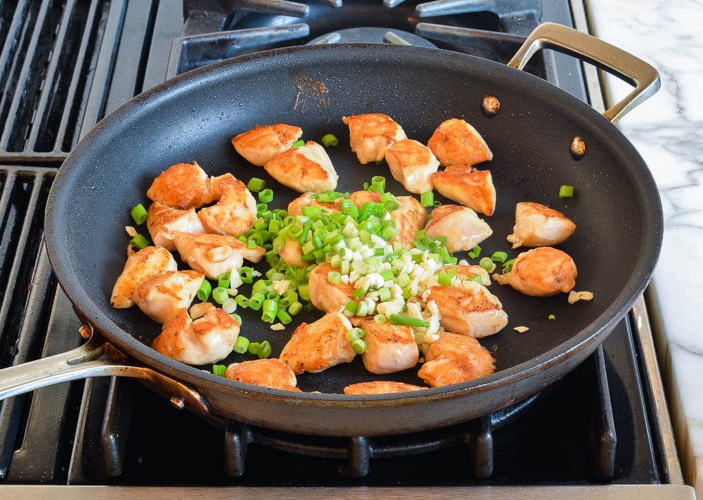 adding scallions and garlic to browned chicken in skillet.