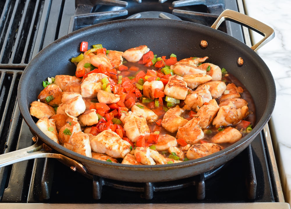 chicken cooking with sauce and veggies in skillet.