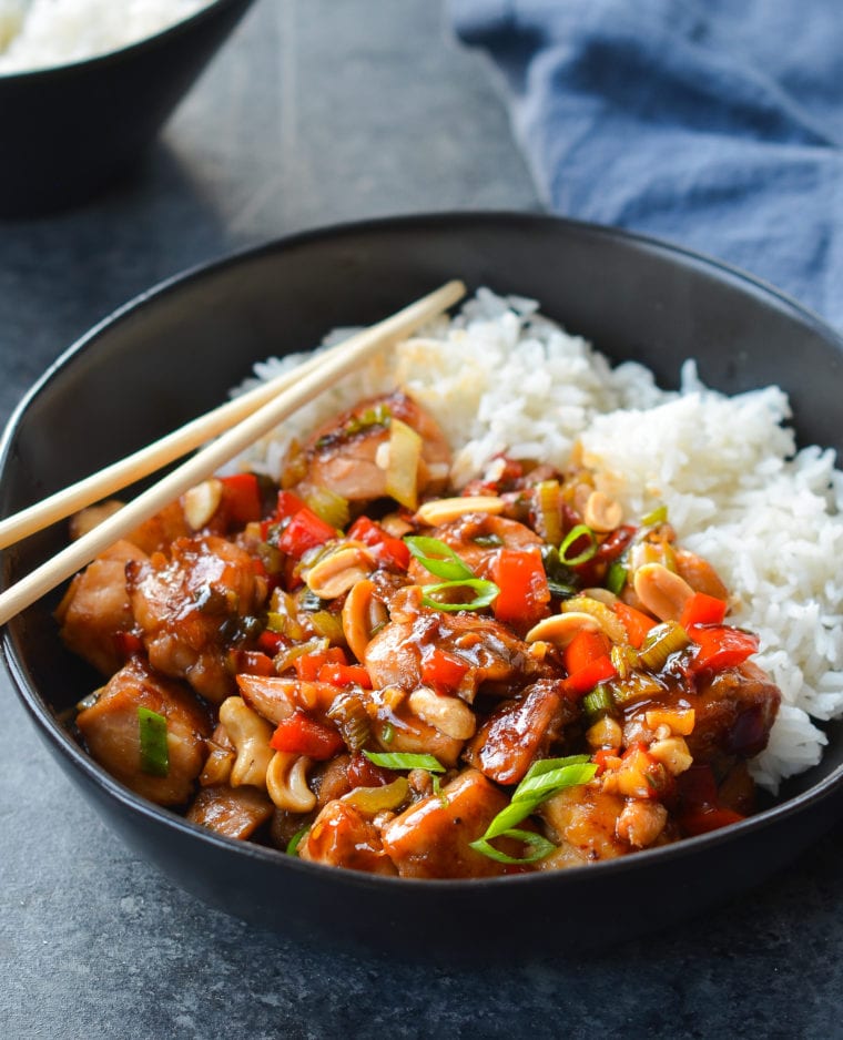 Bowl of Kung Pao chicken over rice with chopsticks.