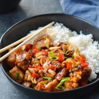 Chopsticks on a bowl of Kung Pao chicken with rice.