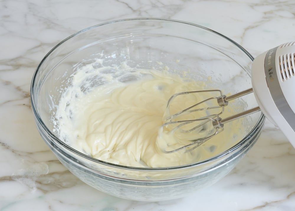 Electric mixer in a bowl with a cream cheese mixture.