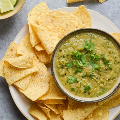 Bowl of salsa verde on a plate with tortilla chips.