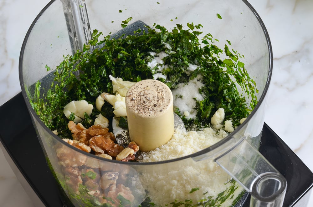 Walnuts, garlic, and other ingredients in a food processor with chopped greens.