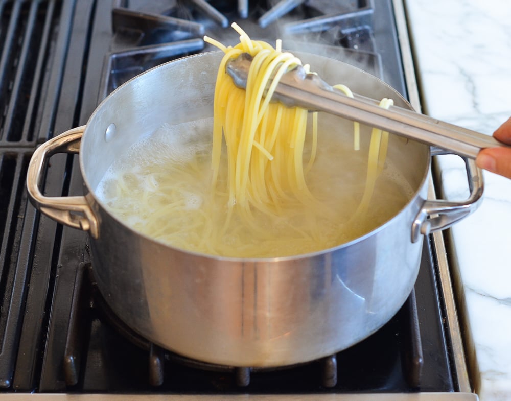 Tongs grabbing noodles from a pot.