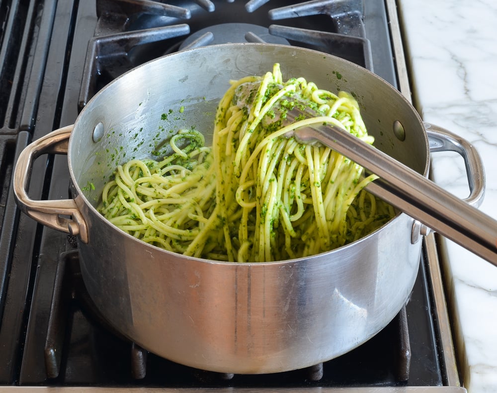 Tongs tossing Spaghetti with Kale and Walnut Pesto.