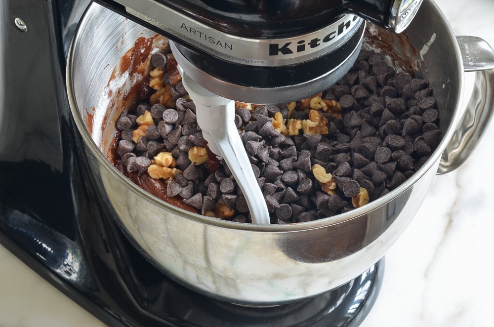 Chocolate chips and nuts in a stand mixer with chocolate batter.
