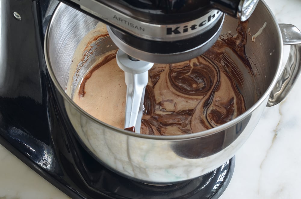 Melted chocolate in a stand mixer with a sugar mixture.