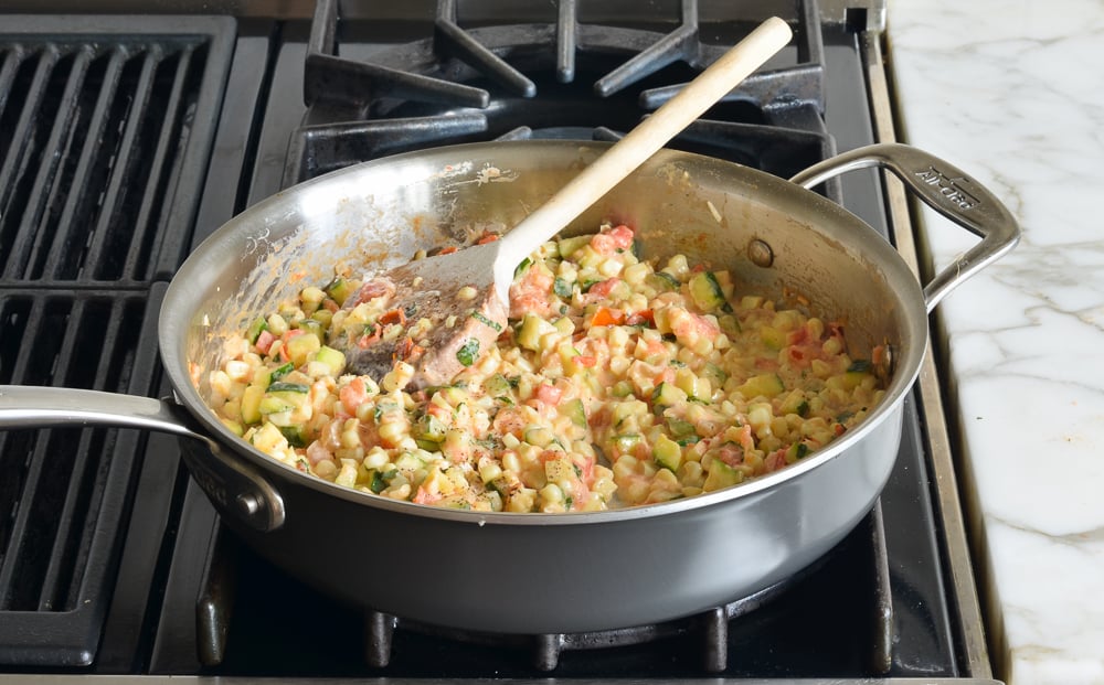 Skillet of creamy corn, zucchini, and tomatoes with goat cheese.