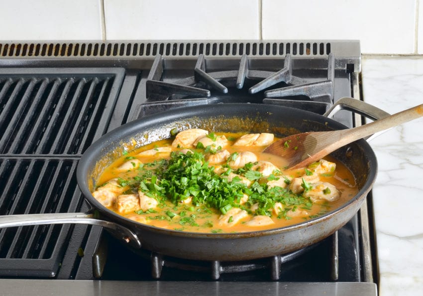 Herbs over a skillet of chicken and coconut milk mixture.