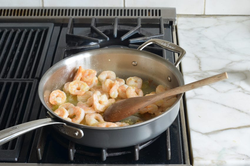 Wooden spoon stirring a pan of shrimp.