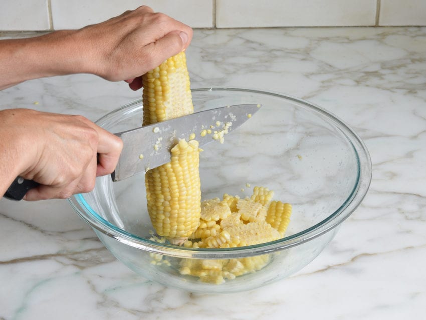 Person using a knife to shave corn off of a cob.