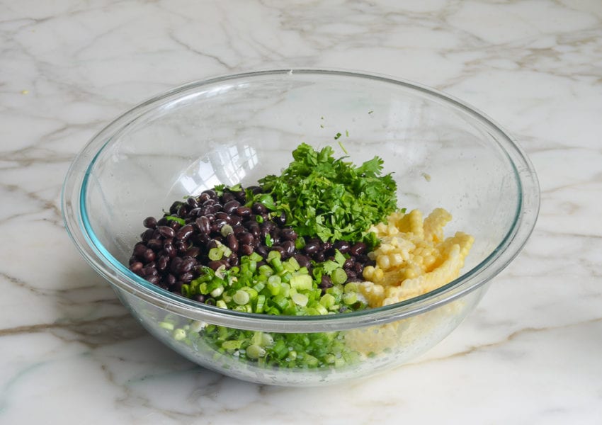 Bowl of unmixed ingredients including black beans, corn, and cilantro.