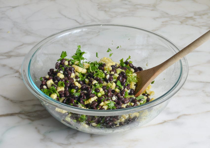 Wooden spoon mixing corn, black beans, scallions, and more.