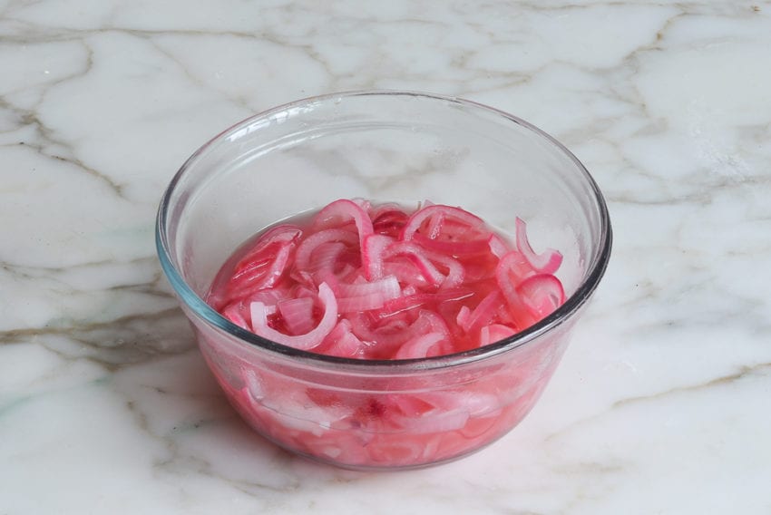 Red onions in pickling liquid in a glass bowl.