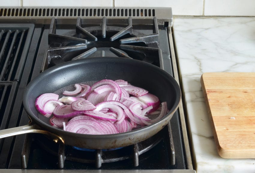 Sliced onions in pickling liquid on a stovetop.