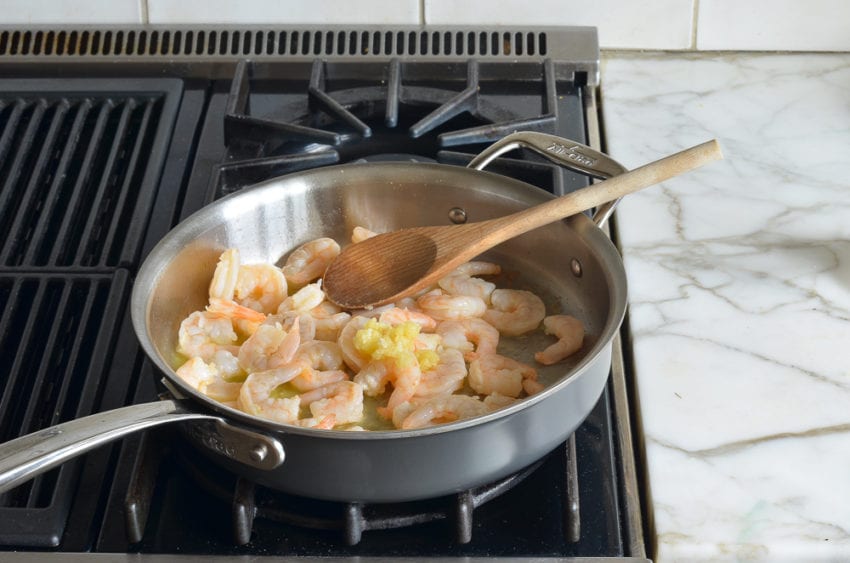 Wooden spoon in a pan with shrimp and garlic.