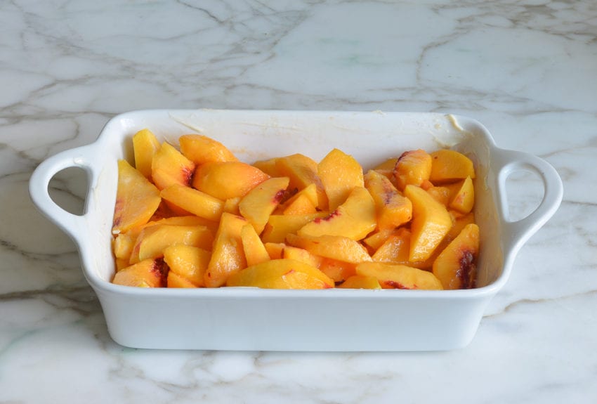 Peaches in a buttered baking dish.