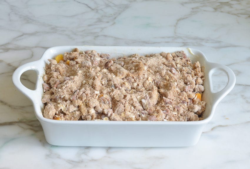 Baking dish of peaches topped with a nut and oat mixture.