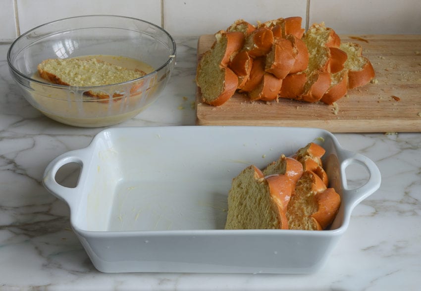 Slice of challah in a bowl of custard next to a baking dish.