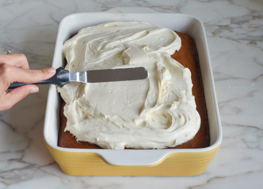Person spreading cream cheese frosting onto a pumpkin cake.
