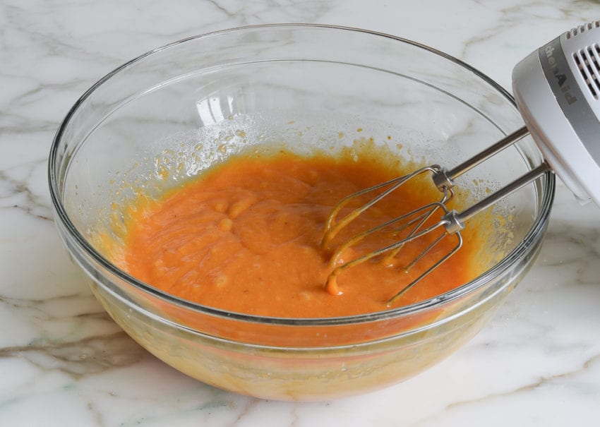 Electric mixer in a bowl with an orange-colored mixture.