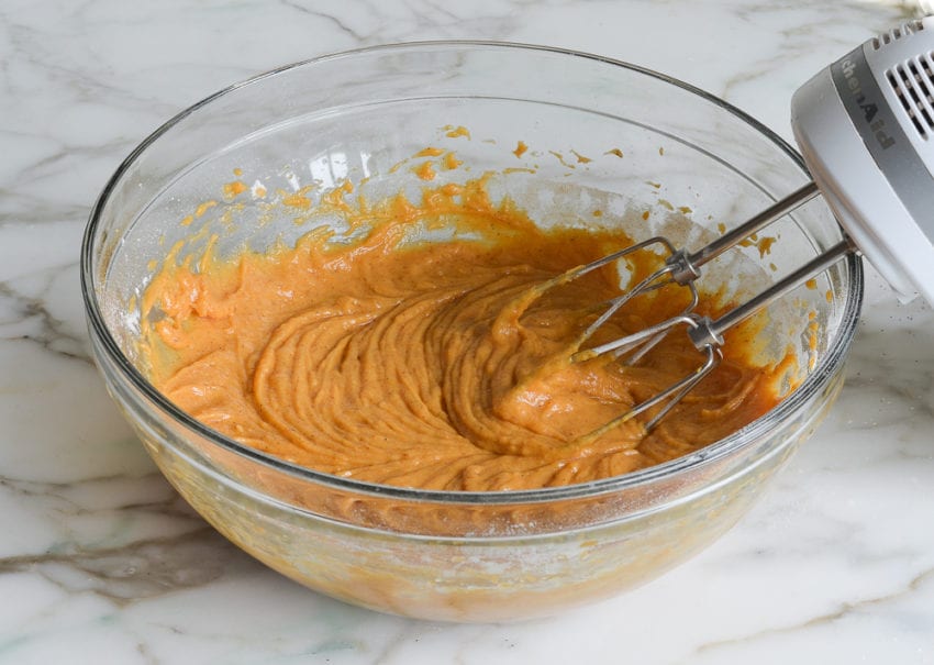 Electric mixer in a bowl with pumpkin cake batter.