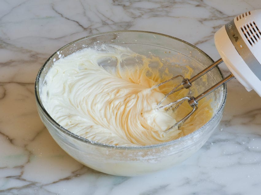 Electric mixer in a bowl with cream cheese frosting.
