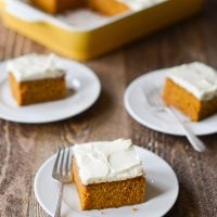 Slices of pumpkin cake with cream cheese frosting on small plates with forks.
