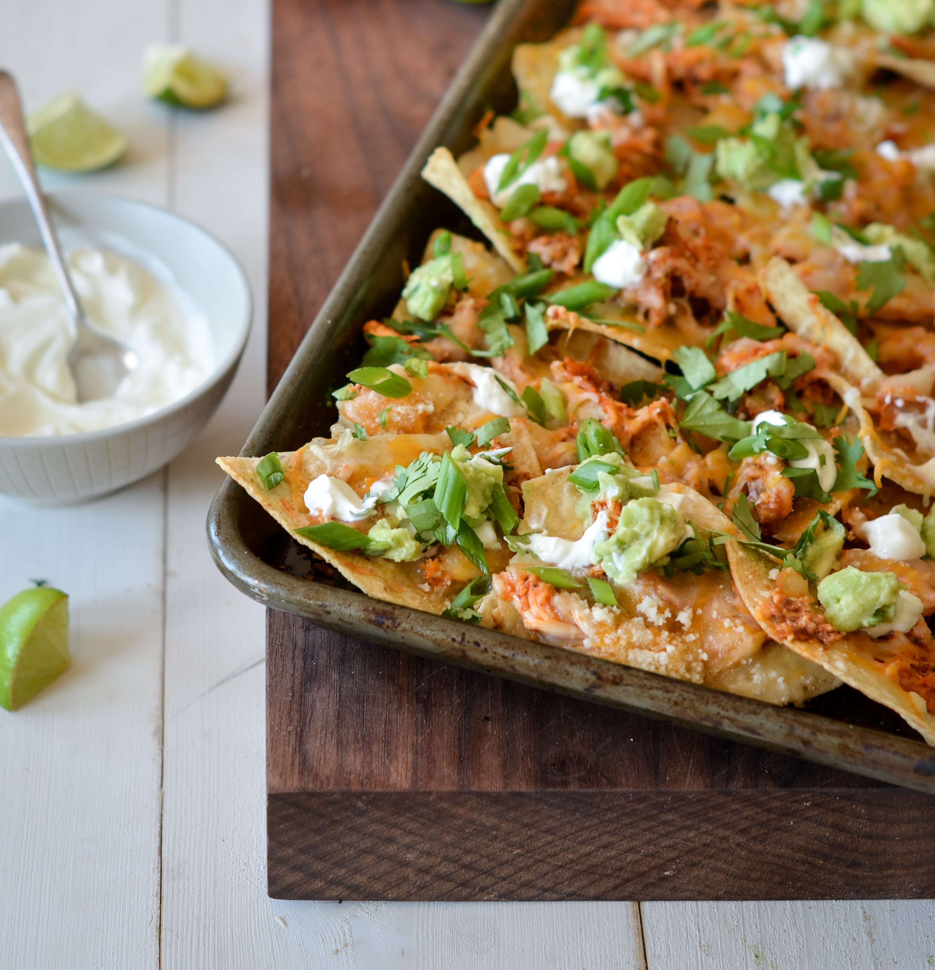 Chicken nachos on a baking sheet with some sour cream on the side.