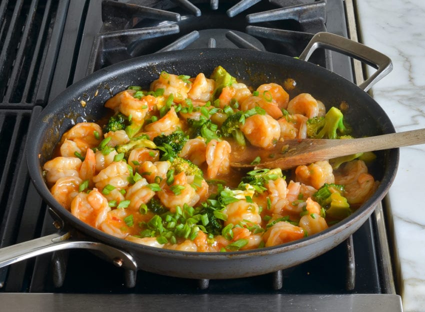 Scallions in a skillet with a shrimp and broccoli mixture.