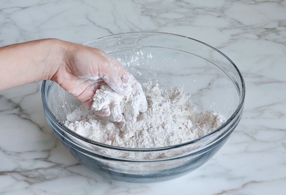Hand rubbing butter into dry ingredients in a bowl.